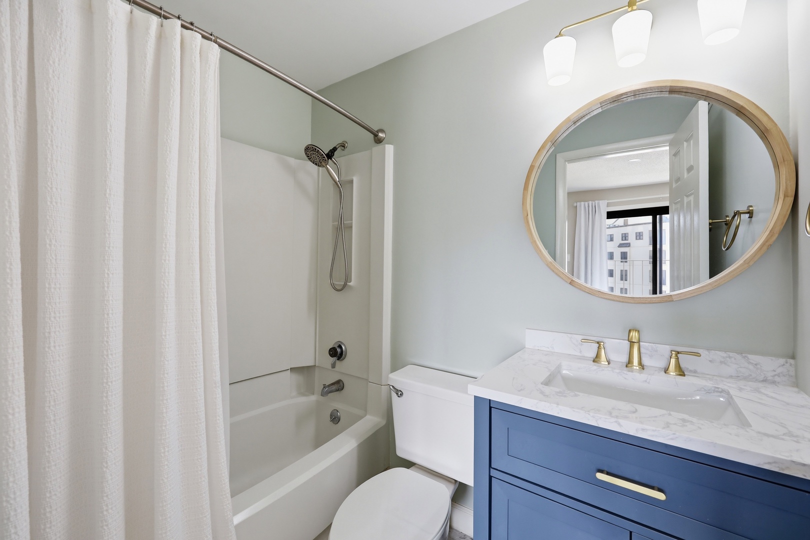 Step into a beautifully refreshed bathroom featuring soft coastal hues, a spacious tub-shower combo, elegant marble vanity, and warm lighting to start your day right.