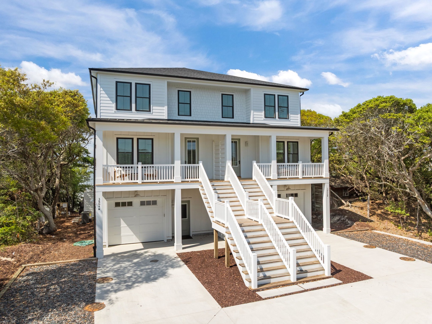 Modern coastal home featuring elevated design with covered porch and garage parking, nestled among mature trees.