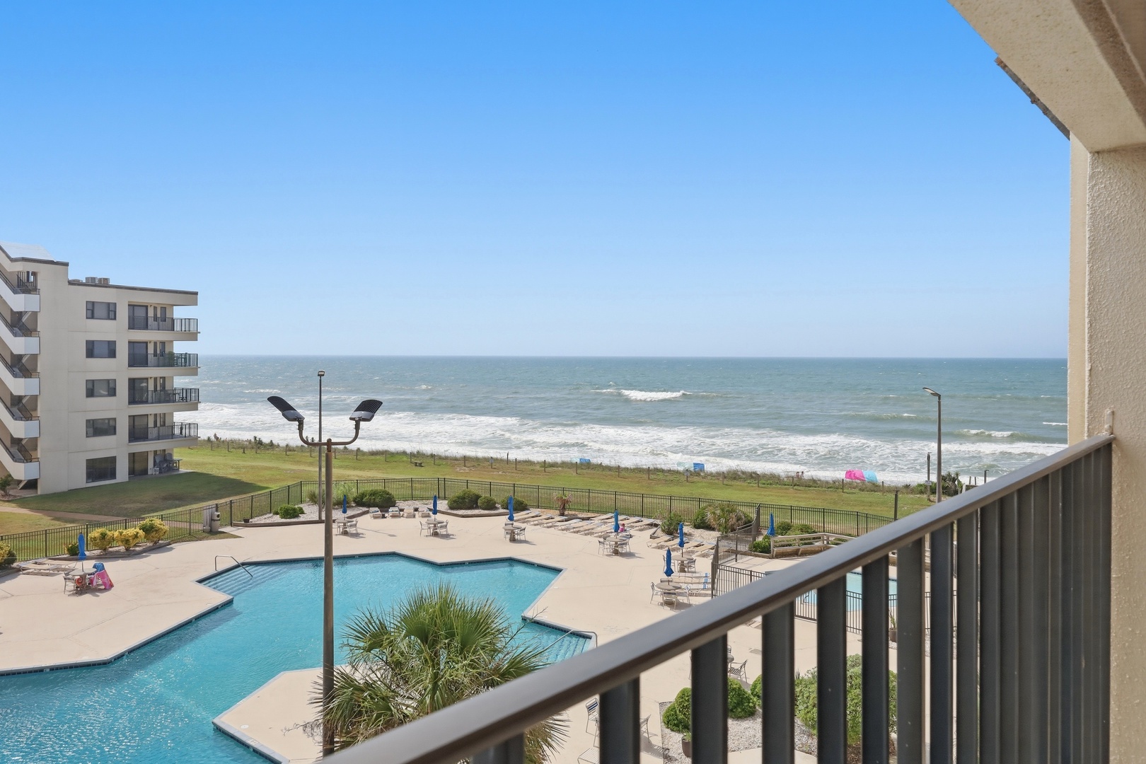 Beachfront property offers direct ocean access, an outdoor pool, and coastal resort ambiance with adjacent buildings and green lawn areas.