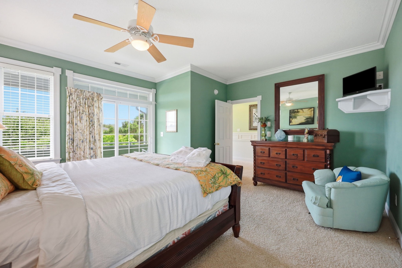Unwind in your peaceful bedroom with soothing sage-green walls, a plush king bed, and a cozy chair. Large windows invite natural light and tropical breezes from your private balcony.