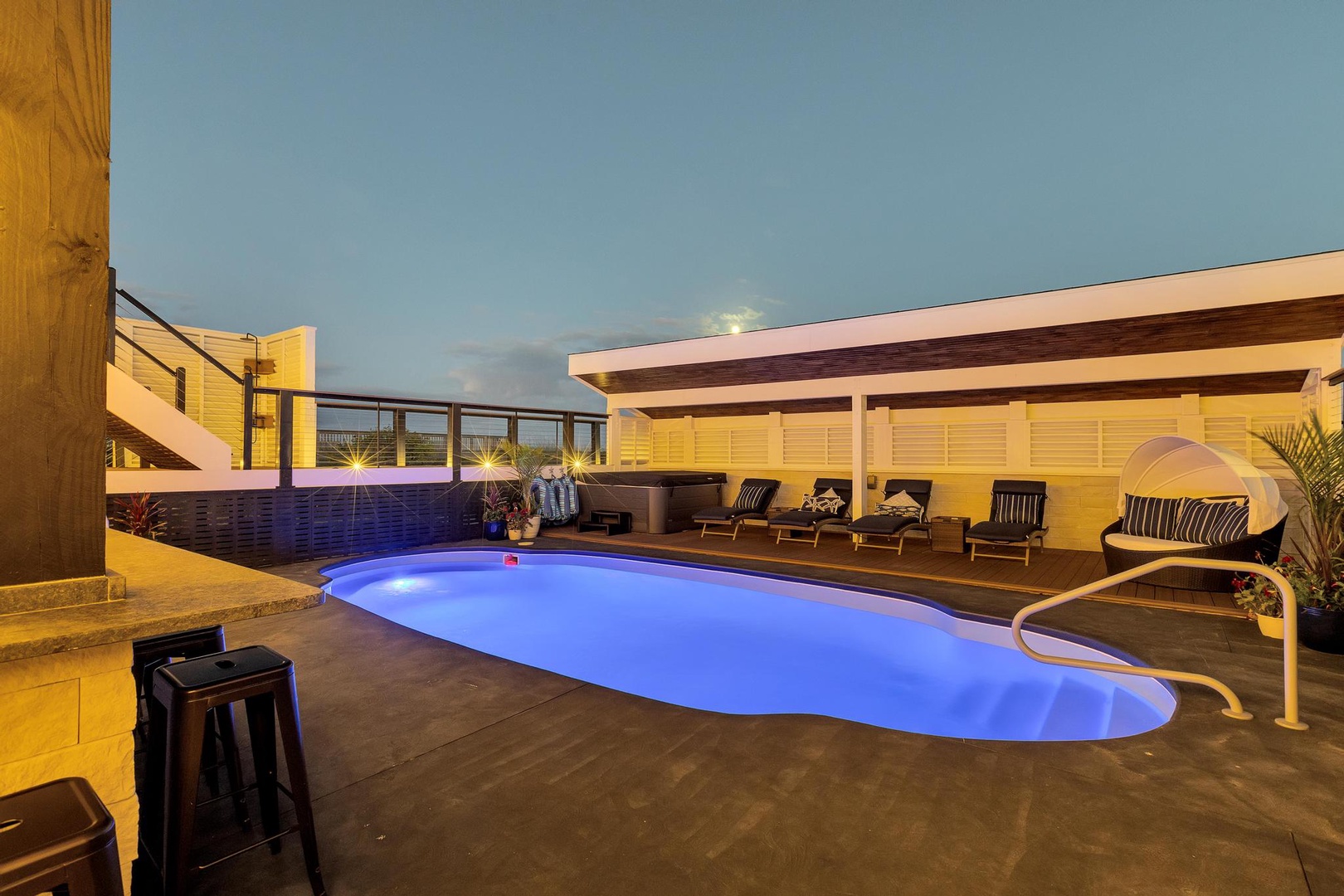 Modern vacation rental with illuminated pool, lounge seating, and a covered pavilion capturing golden-hour glow beneath a serene evening sky.