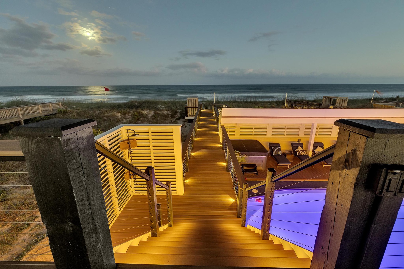 A beachfront multilevel deck with ambient lighting leads to the sandy shore and ocean. This elevated outdoor space features lounging areas and direct beach access for coastal relaxation.
