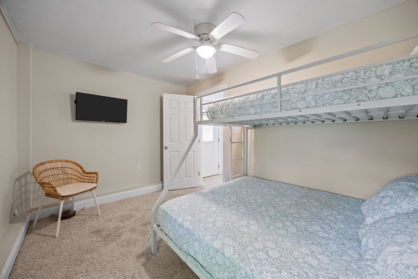 Your cozy bedroom features comfortable bunk beds with soft blue linens, a ceiling fan for cool nights, and modern amenities like a wall-mounted TV.