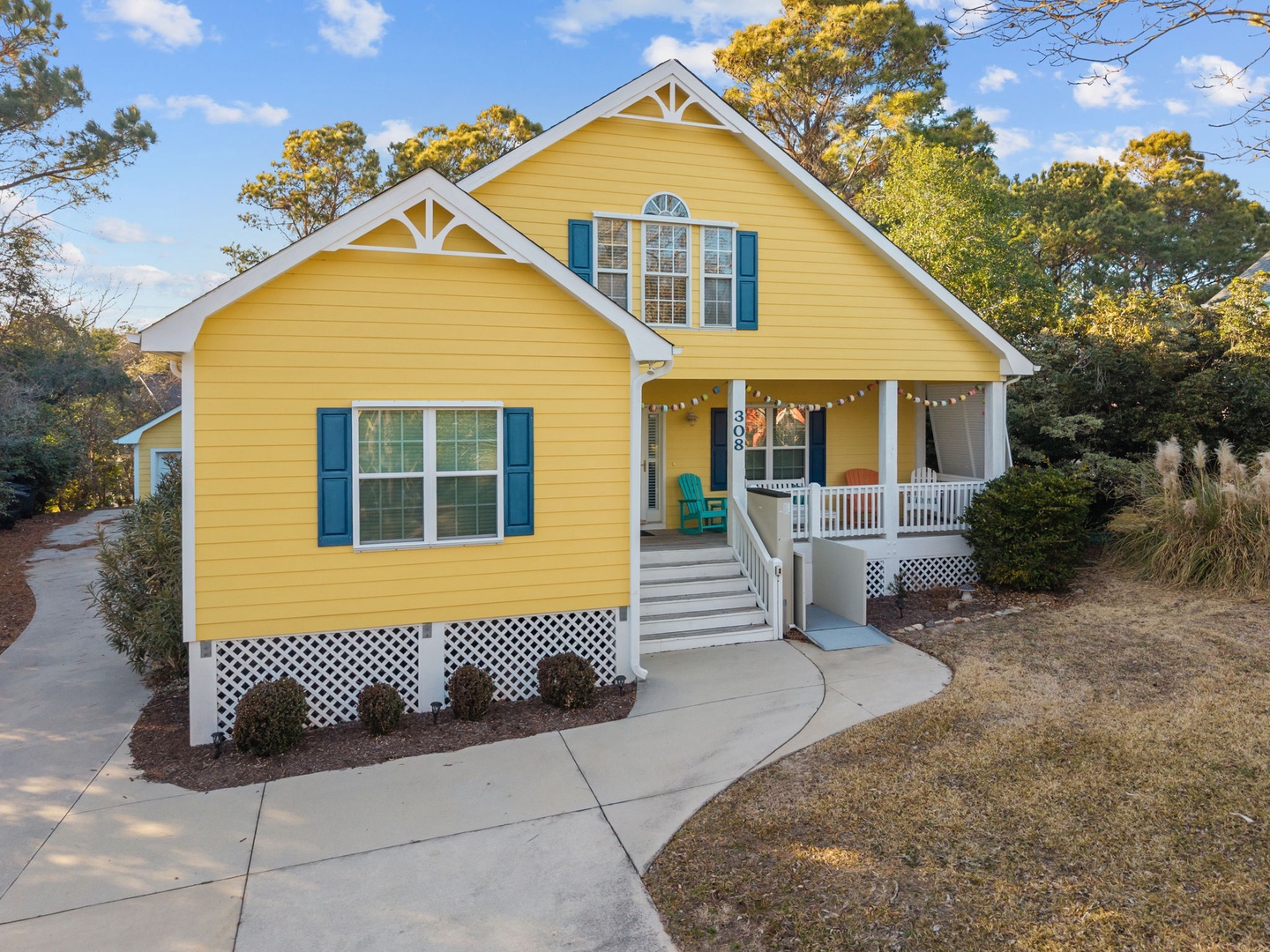Charming yellow cottage with cheerful blue shutters and welcoming front porch, nestled among mature trees in a peaceful residential setting.