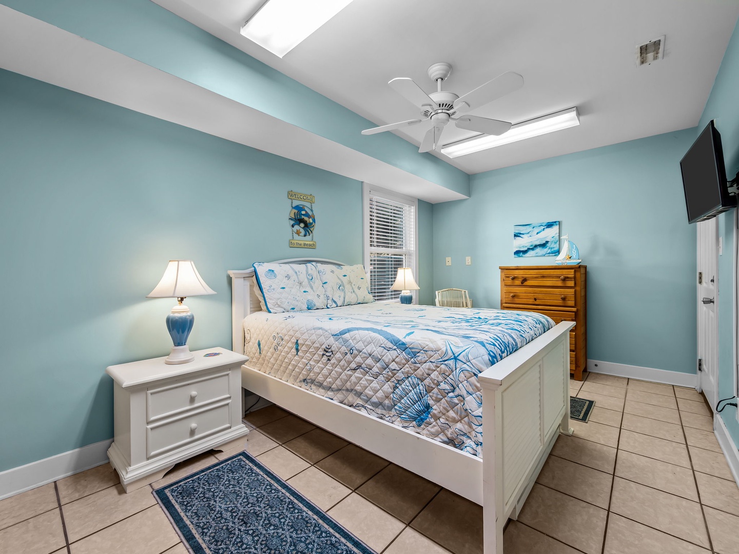 Unwind in your coastal-themed bedroom with aqua walls, ceiling fan breeze, and ocean-inspired linens creating a peaceful retreat.