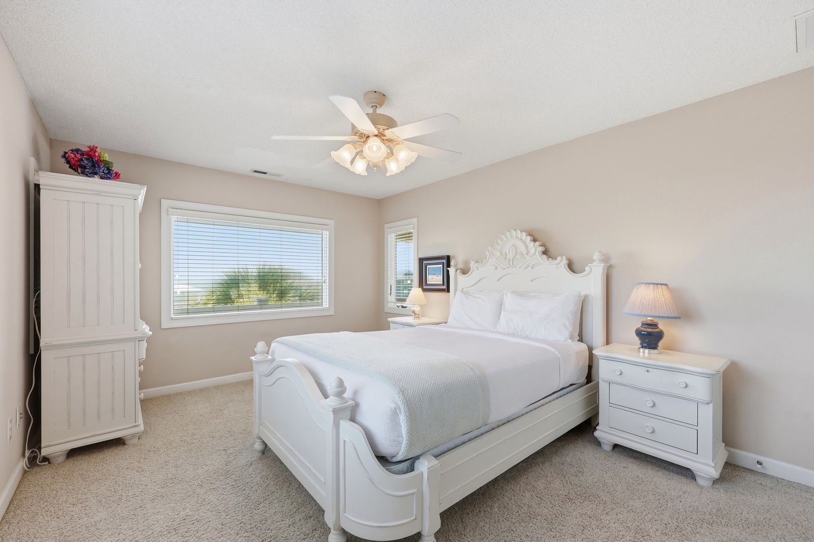 Sink into crisp white linens under soft ceiling fan light. Your elegant white bedroom offers peaceful views and ample storage for a restful coastal retreat.