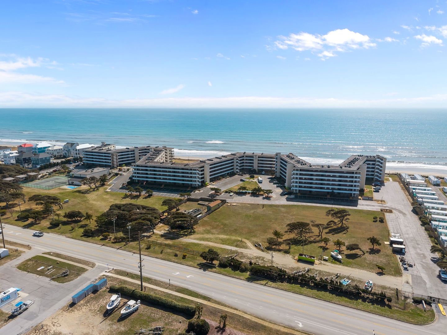 Beachfront property complex situated along pristine coastline with direct access to sandy shores and turquoise waters, surrounded by green spaces and coastal parkland.