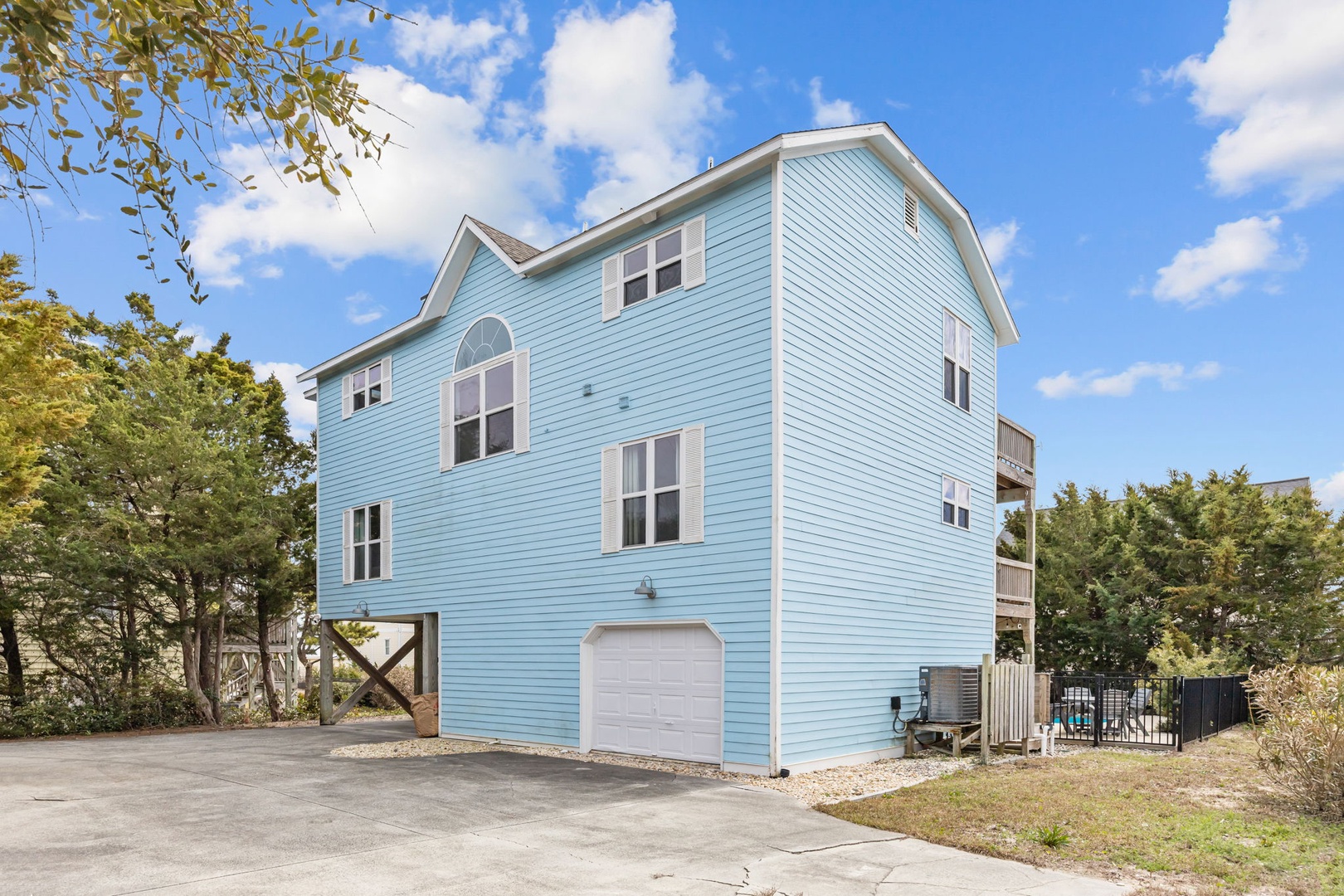 Charming blue beach house with elevated design, garage parking, and mature landscaping creates the perfect coastal retreat setting.