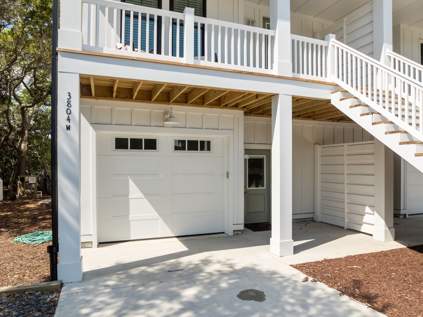 Charming beach house exterior with covered parking and upper deck balcony surrounded by coastal trees.