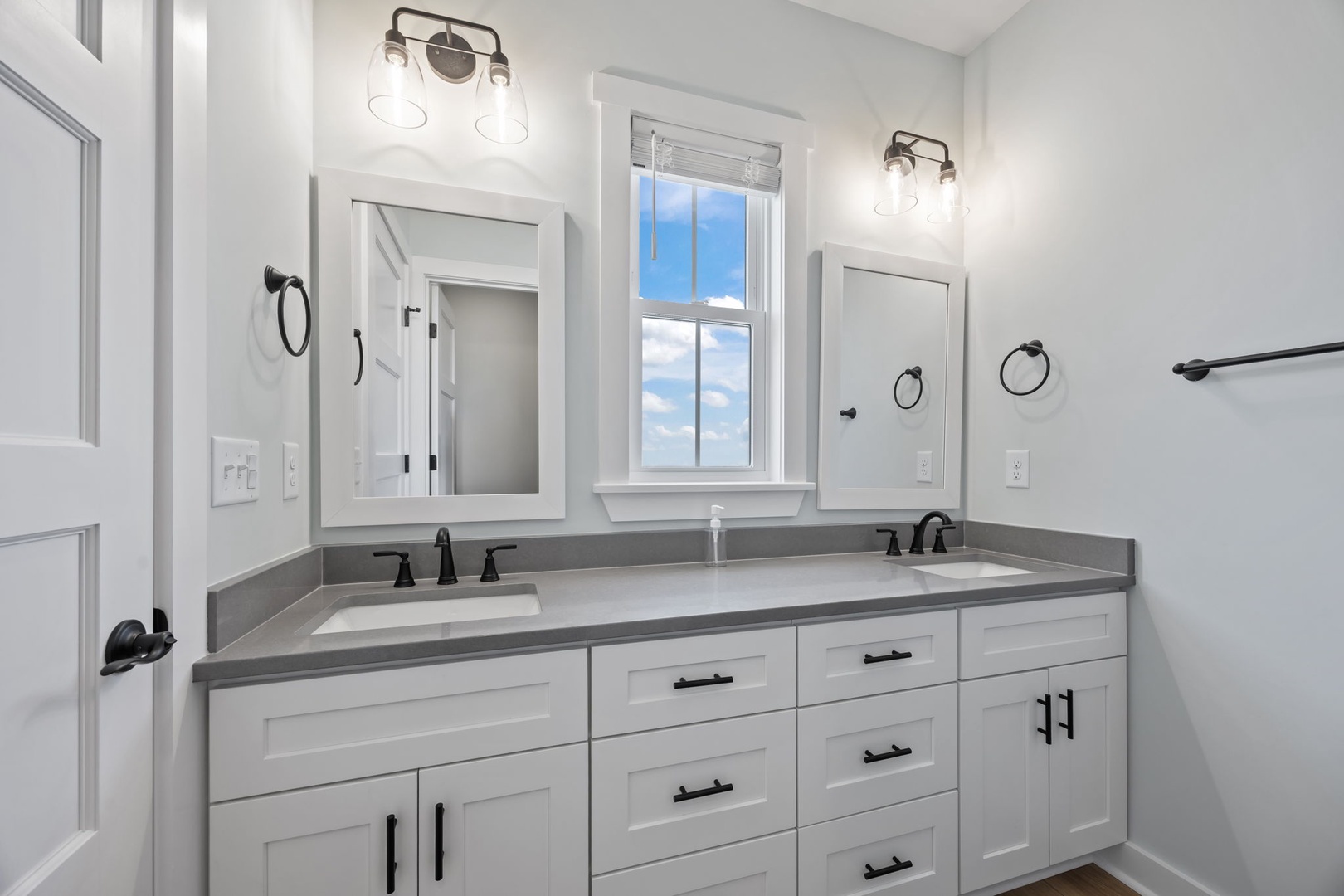Your spacious dual-vanity bathroom features gleaming quartz countertops and crisp white cabinetry, perfectly lit for your morning routine.