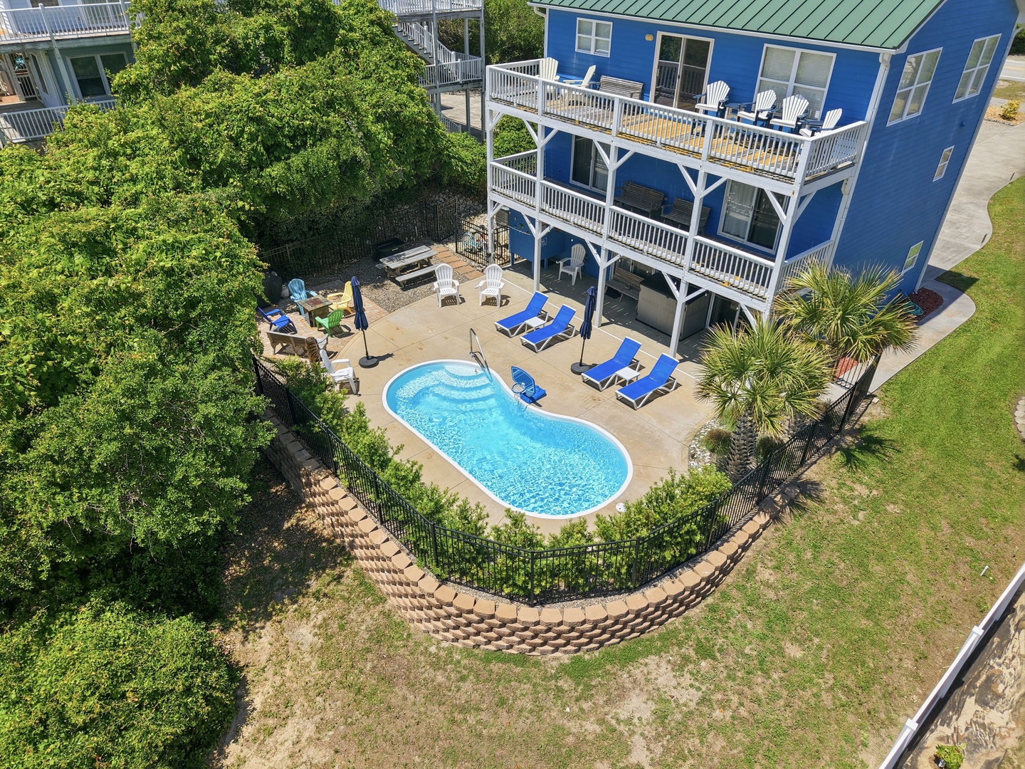 Aerial view of the vibrant blue property featuring a private kidney-shaped pool surrounded by sunbeds and lush greenery, perfect for a coastal getaway.