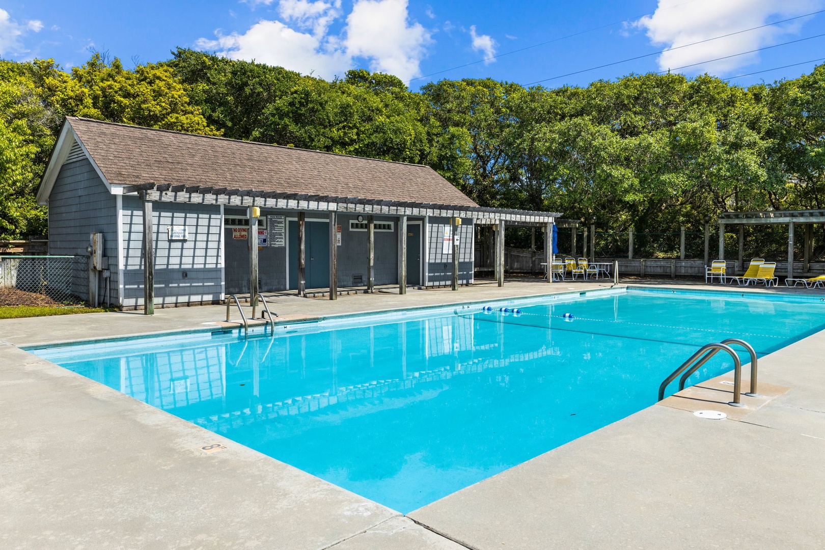 Community swimming pool with poolside building and changing facilities surrounded by lush greenery.
