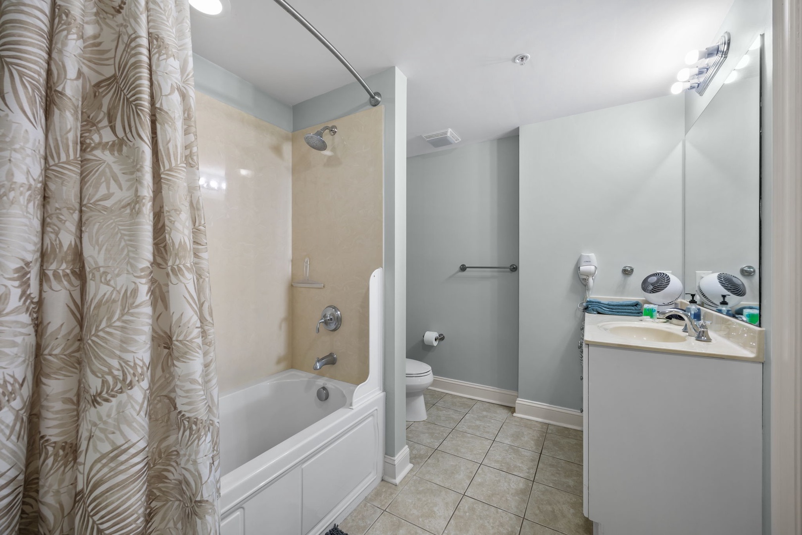 Step into your peaceful bathroom retreat featuring a relaxing tub-shower combo, modern vanity, and tropical-patterned curtains for your comfort.
