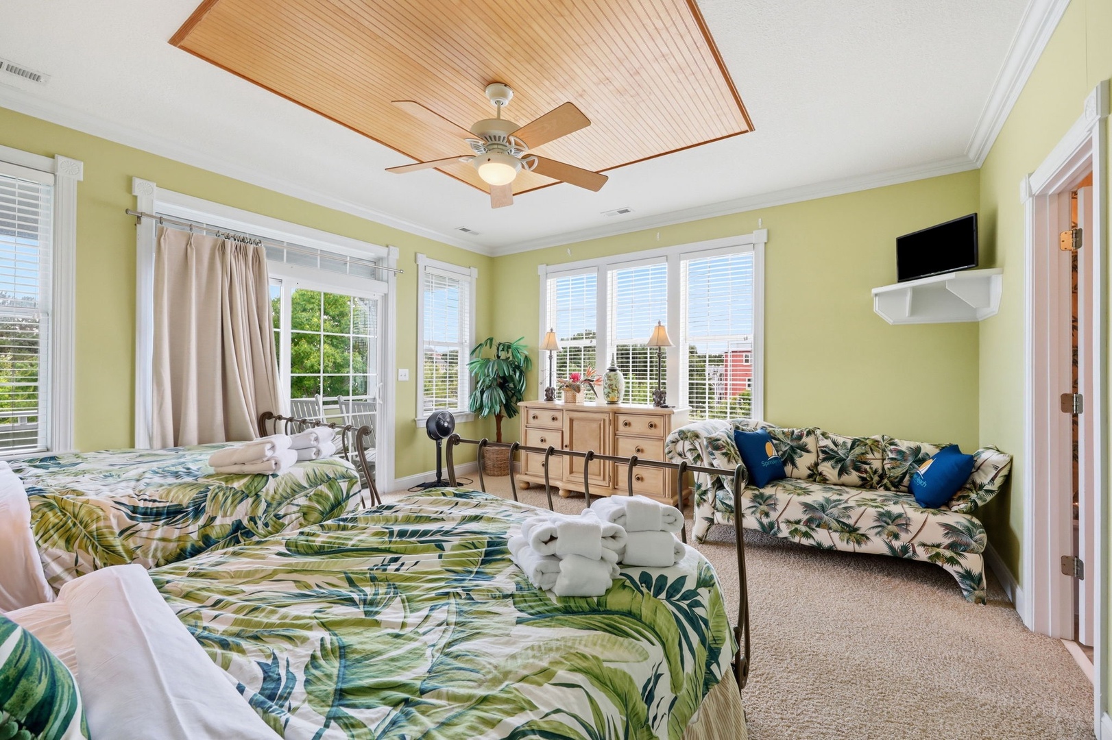Your tropical-inspired retreat features two plush beds and a cozy seating area, where natural light streams through multiple windows. Drift to sleep under the warm glow of the ceiling fan, surrounded by lush palm-printed linens.