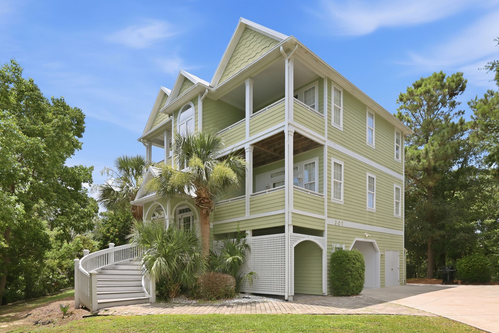 This charming coastal-style property sits nestled among lush trees and tropical palms, offering a private entrance and a welcoming staircase that leads to beautifully appointed living spaces throughout multiple levels.