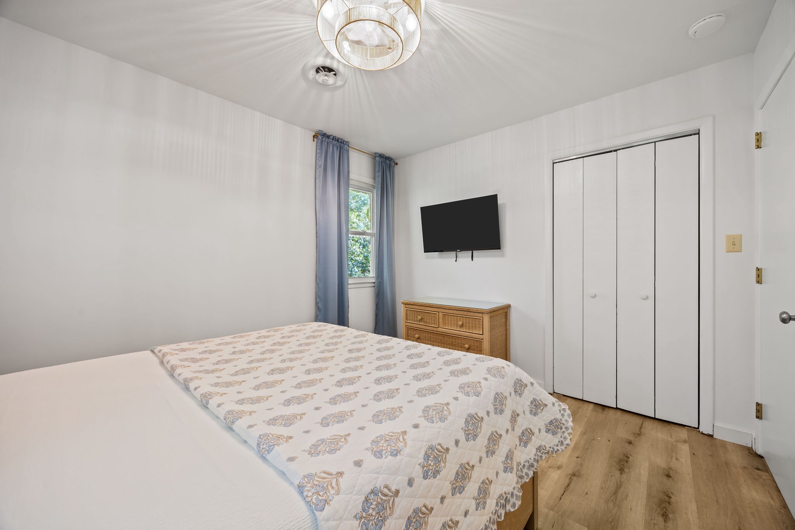 Unwind in your peaceful bedroom featuring a comfortable bed, modern TV, and elegant chandelier for the perfect night's rest.