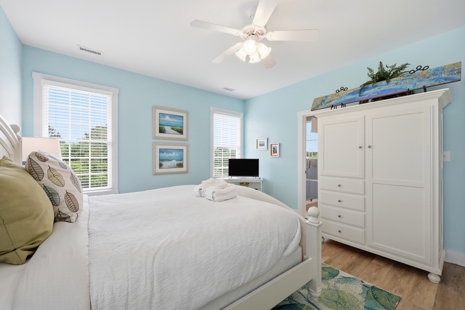 Drift off in your coastal-themed bedroom, where soft blue walls and crisp linens create a serene retreat. Natural light pours through the windows, while the ceiling fan keeps you cool and comfortable.