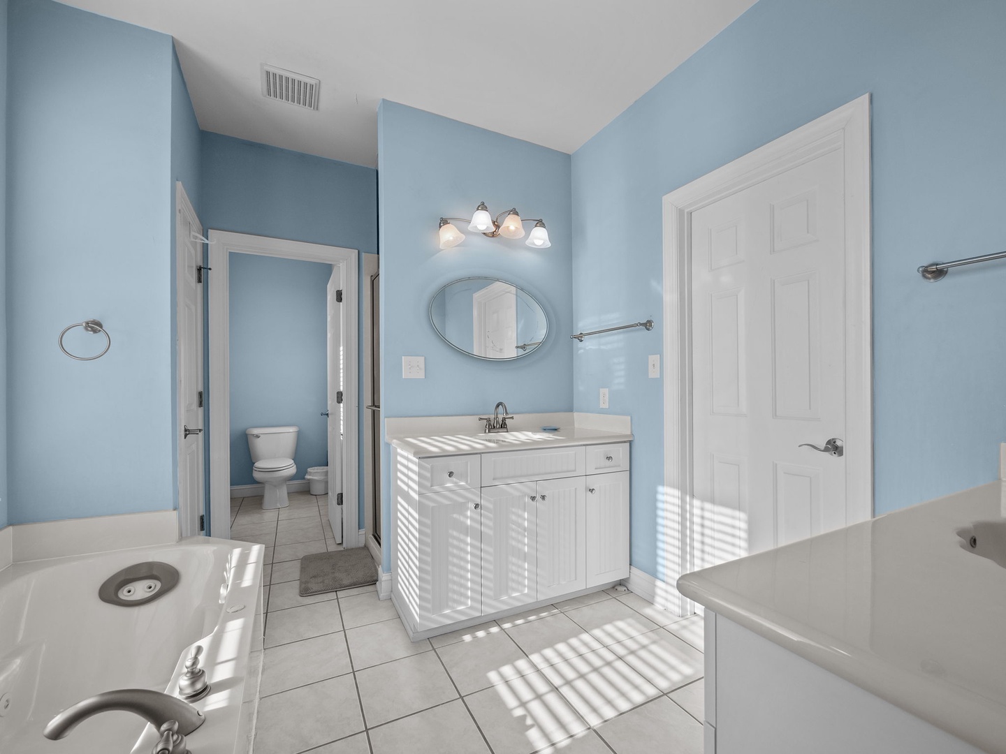 Freshen up in your spacious bathroom featuring serene blue walls, bright vanity lighting, and a relaxing soaking tub.