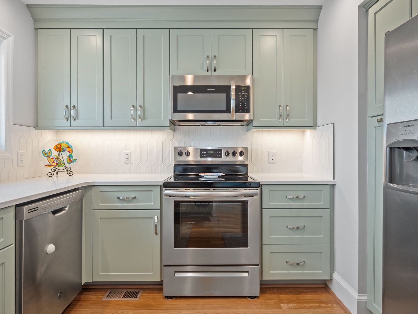 Step into your fully-equipped kitchen with sage-green cabinets, stainless steel appliances, and charming details that make cooking feel like home.