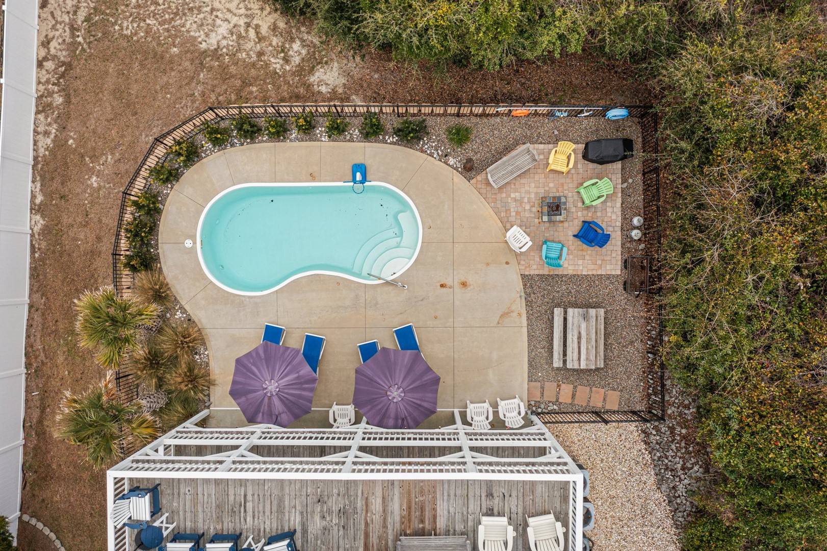 Aerial view of vacation rental property featuring kidney-shaped swimming pool with patio seating, umbrellas, and natural landscaping throughout the grounds.