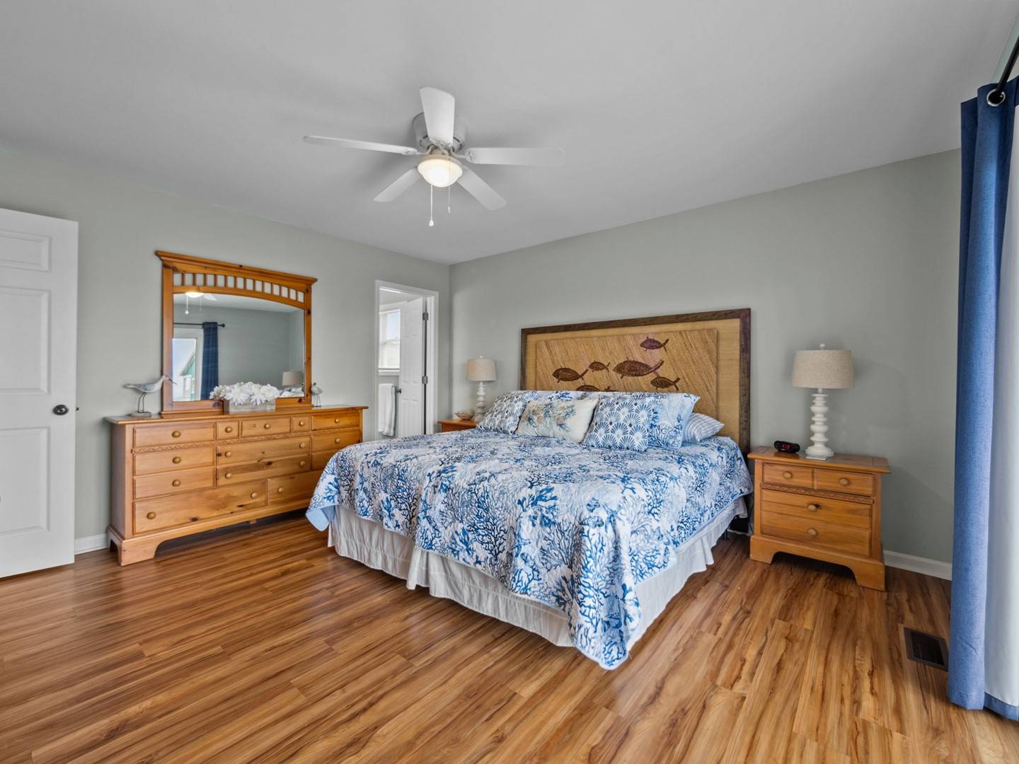 Drift off in your spacious bedroom with gleaming hardwood floors, coastal blue linens, and a gentle ceiling fan creating the perfect sleeping sanctuary.
