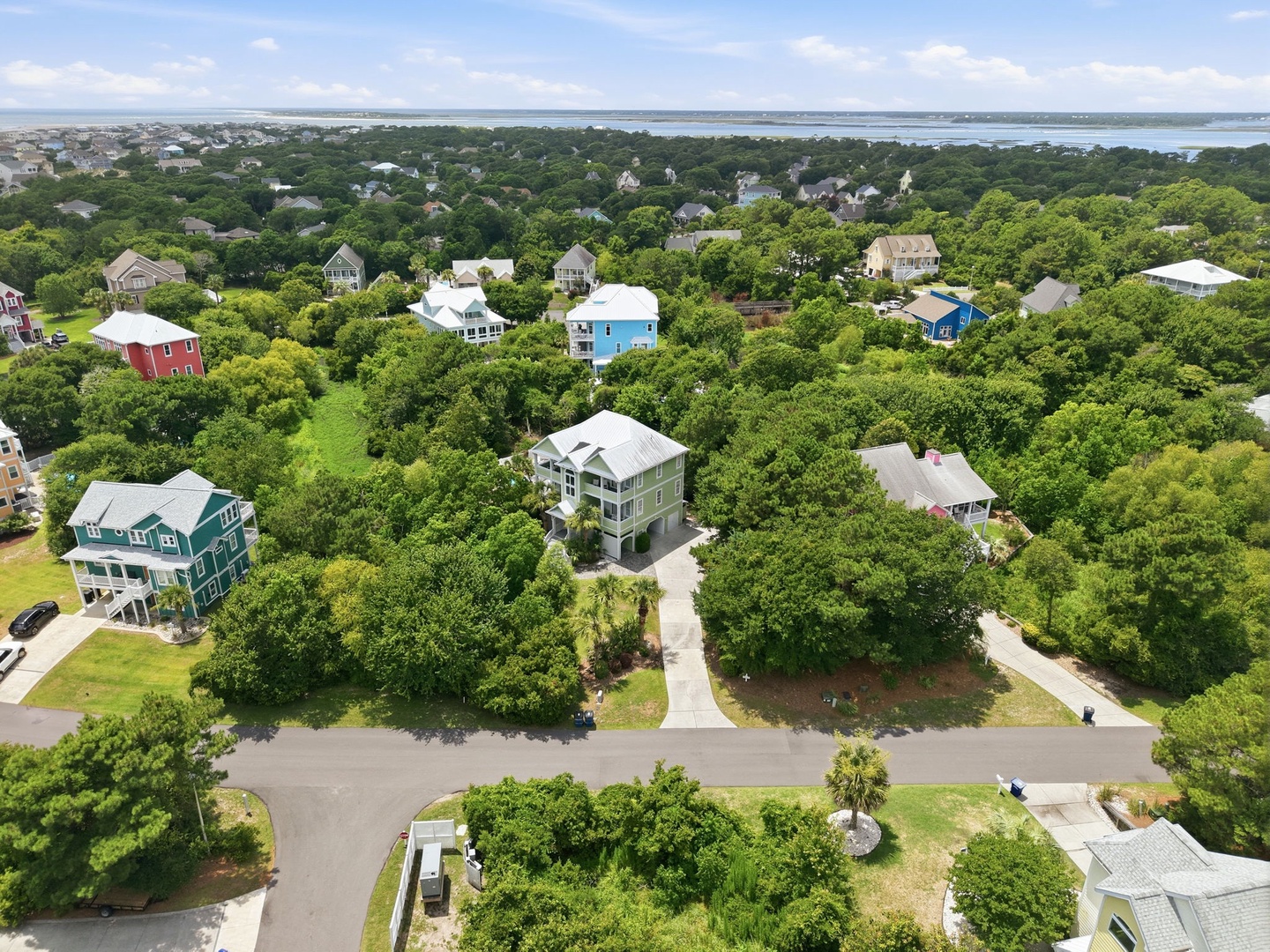 Aerial view of a coastal residential neighborhood nestled among lush trees with waterfront views, showcasing the property's peaceful location near the shore.