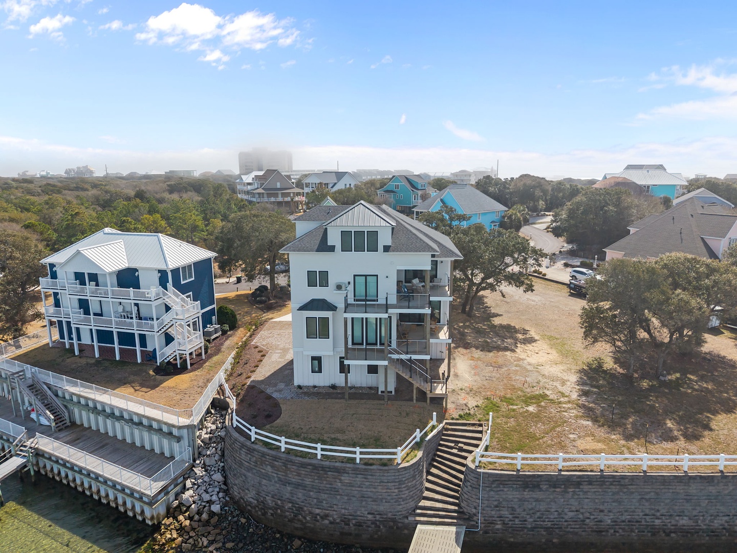 Waterfront vacation homes nestled among coastal trees with private docks and sandy paths leading to the shore.