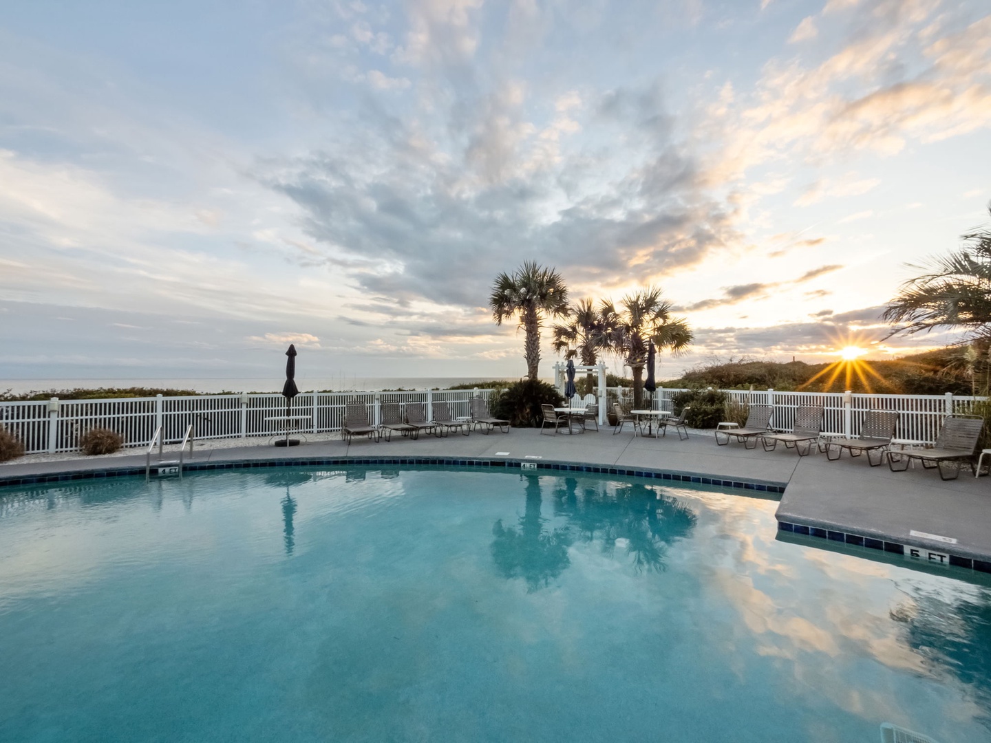 Beautiful poolside sunset with palm trees and outdoor seating creating the perfect evening atmosphere.