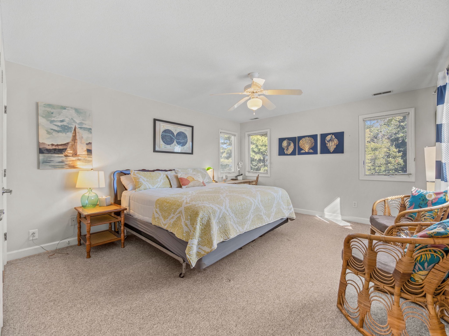Relax in your coastal-themed bedroom with charming nautical artwork, cozy reading chairs, and gentle ceiling fan keeping you comfortable.
