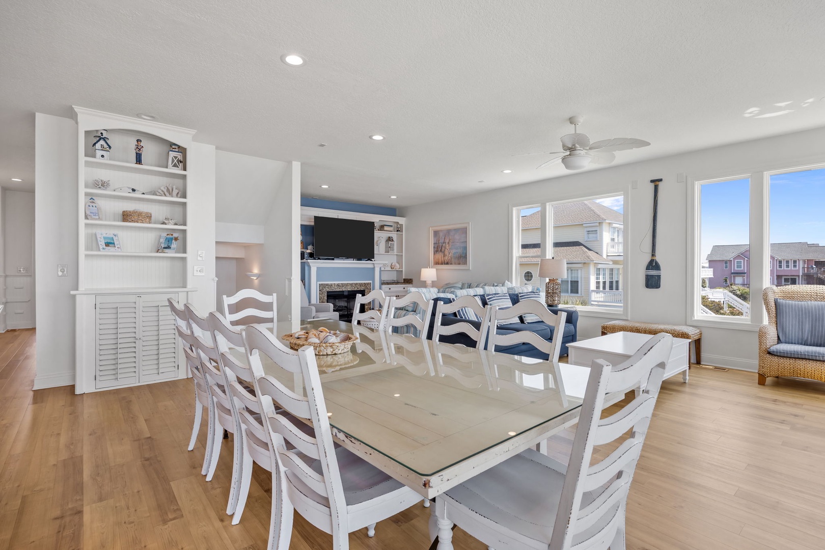Your bright dining space flows seamlessly into the living area, where white coastal furnishings and built-in entertainment center create perfect gathering spots.