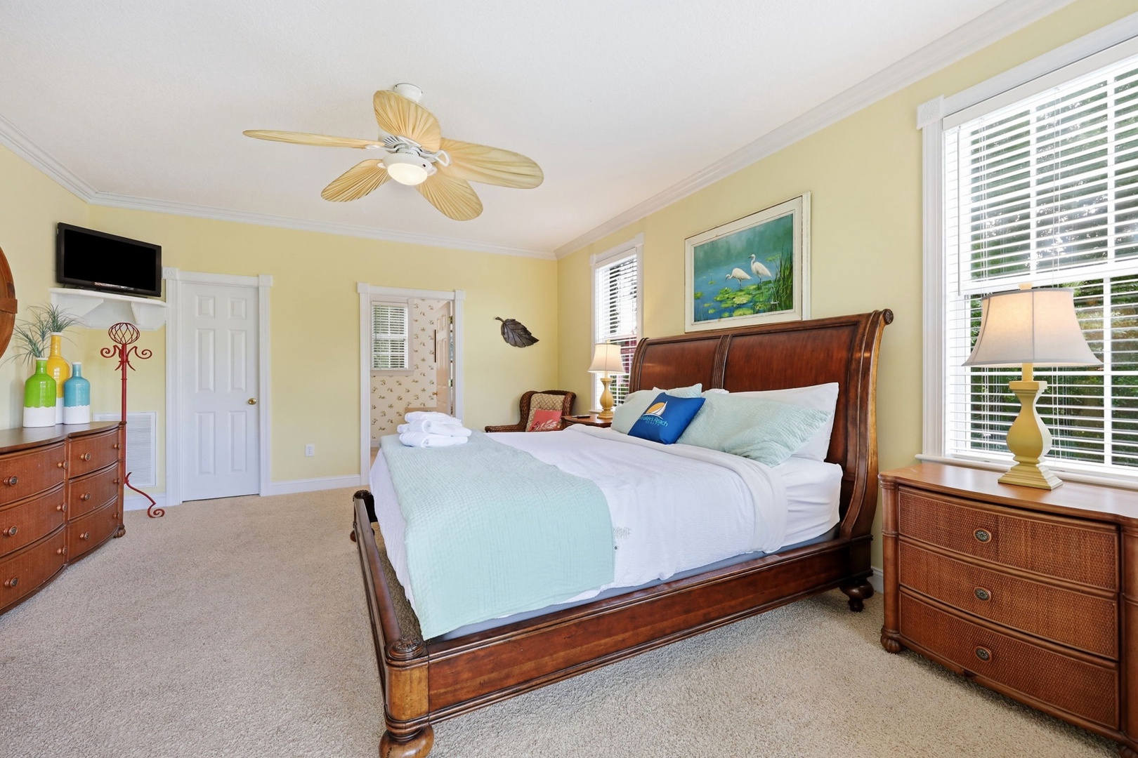 Your coastal-inspired bedroom awaits with plush bedding, soothing yellow walls, and tropical ceiling fan. Unwind in this serene retreat designed for restful nights and relaxed mornings.