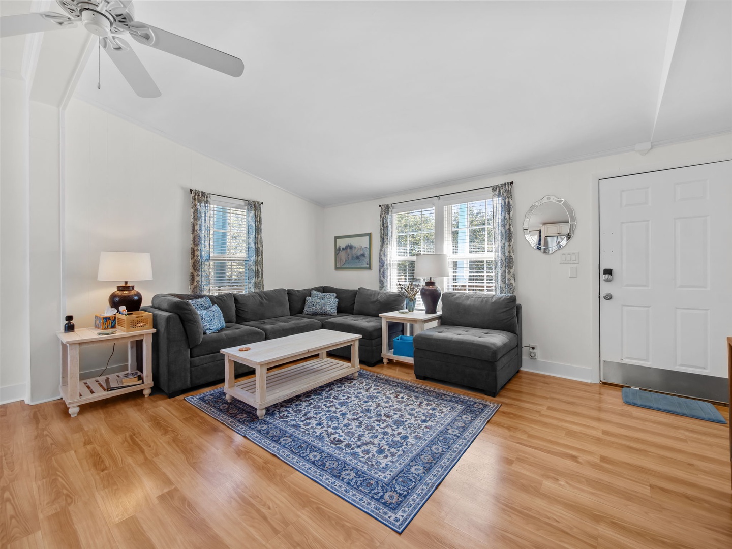 Unwind on the plush sectional sofa in your bright, airy living room featuring gleaming hardwood floors and charming coastal decor.