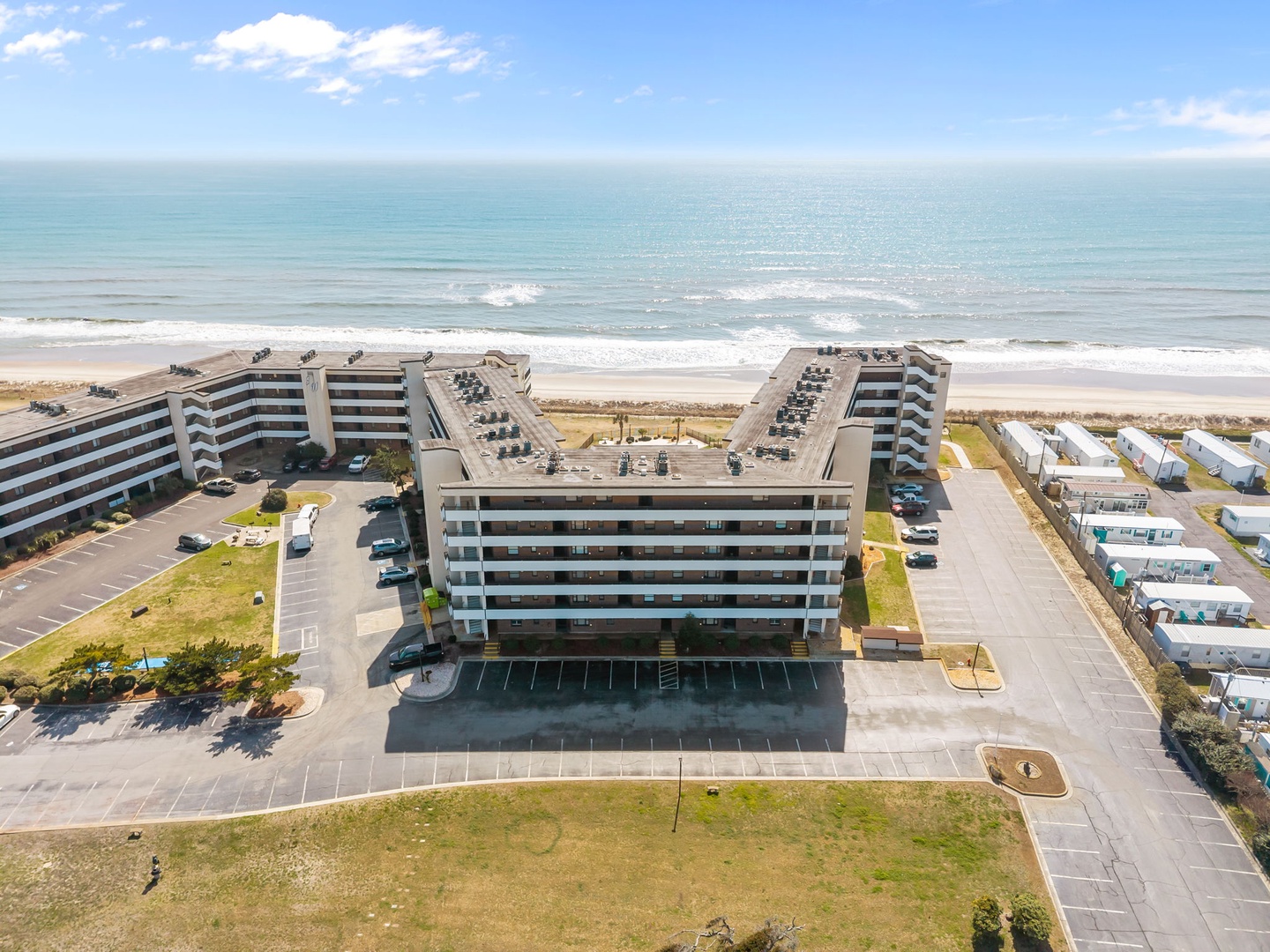 Beachfront property featuring multiple buildings with direct ocean access, parking areas, and nearby accommodations along a pristine sandy shoreline under clear blue skies.
