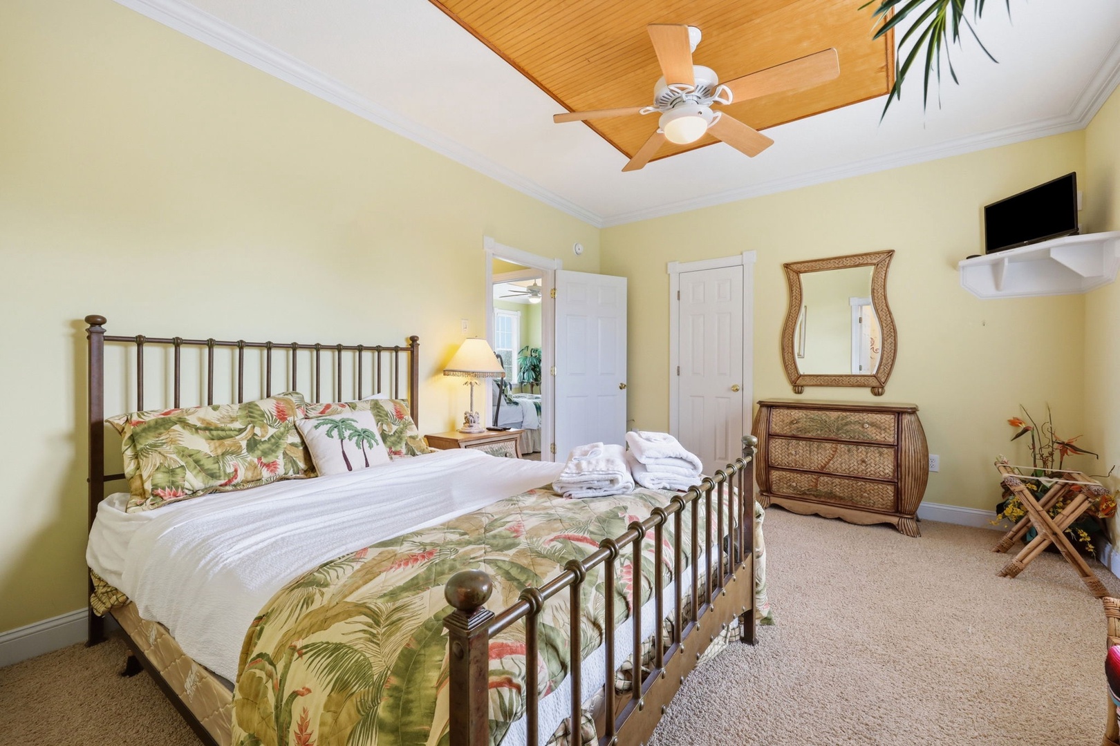Your sunny retreat features a tropical-themed bed with lush botanical linens, a cozy tray ceiling with a fan, and island-inspired furnishings that create a peaceful, breezy atmosphere for restful nights.