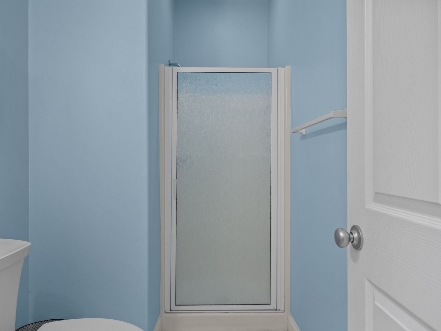 Step into your private bathroom featuring a spacious glass shower enclosure with calming blue walls that create a serene, spa-like atmosphere.