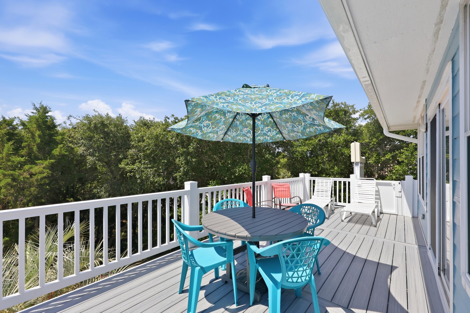 Your private deck awaits with colorful outdoor dining beneath a cheerful umbrella, surrounded by lush greenery and endless blue skies—the perfect spot to savor morning coffee or evening gatherings.