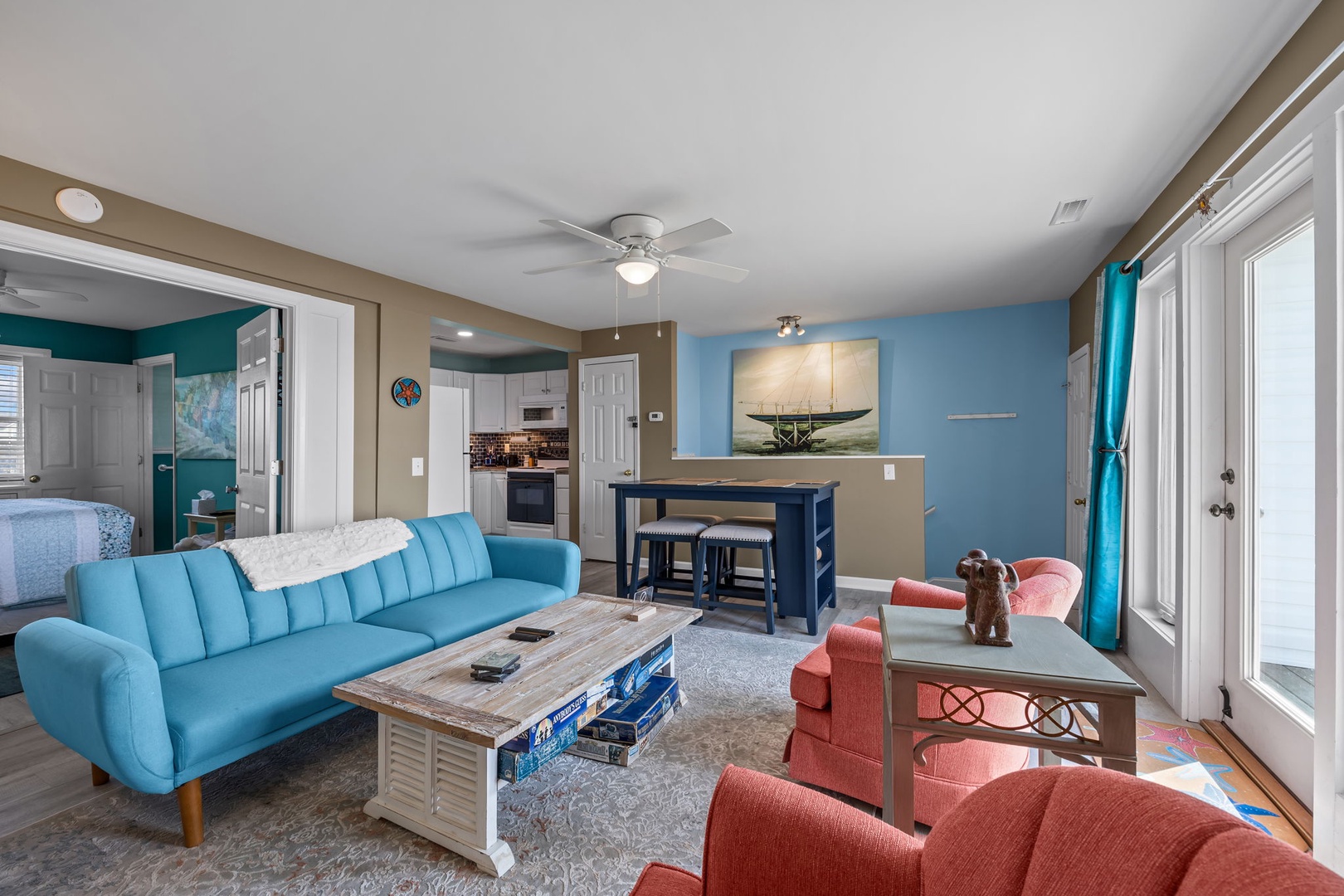 Relax in your bright, coastal-themed living space with comfortable seating, modern kitchen access, and cheerful turquoise accents throughout.