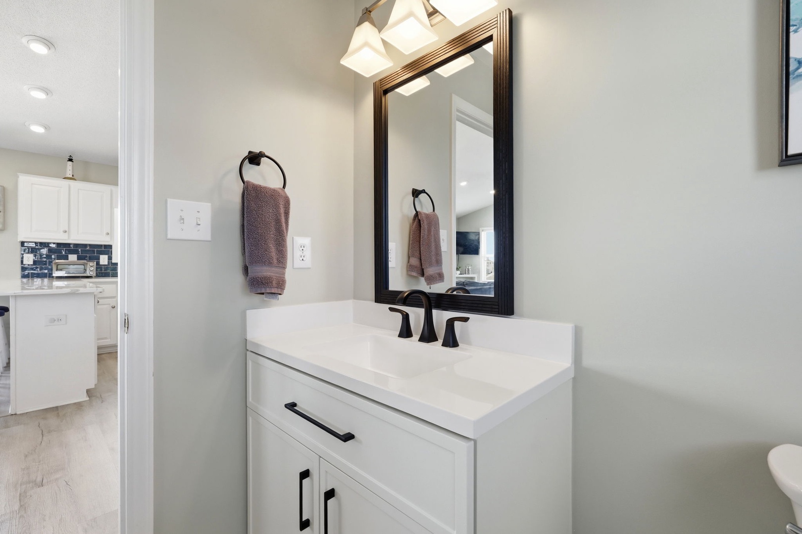 Freshen up in your stylish bathroom featuring a crisp white vanity, framed mirror, and modern fixtures. Soft lighting and thoughtfully placed towels create a welcoming retreat.