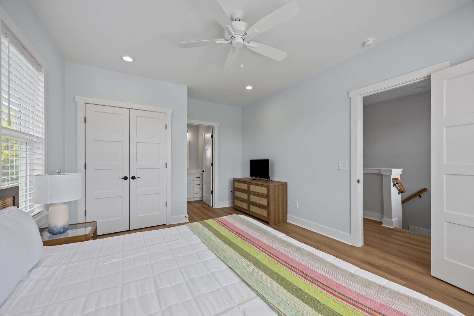 Your airy bedroom features bright natural light, a ceiling fan for comfort, and a colorful striped rug adding warmth to the clean design.
