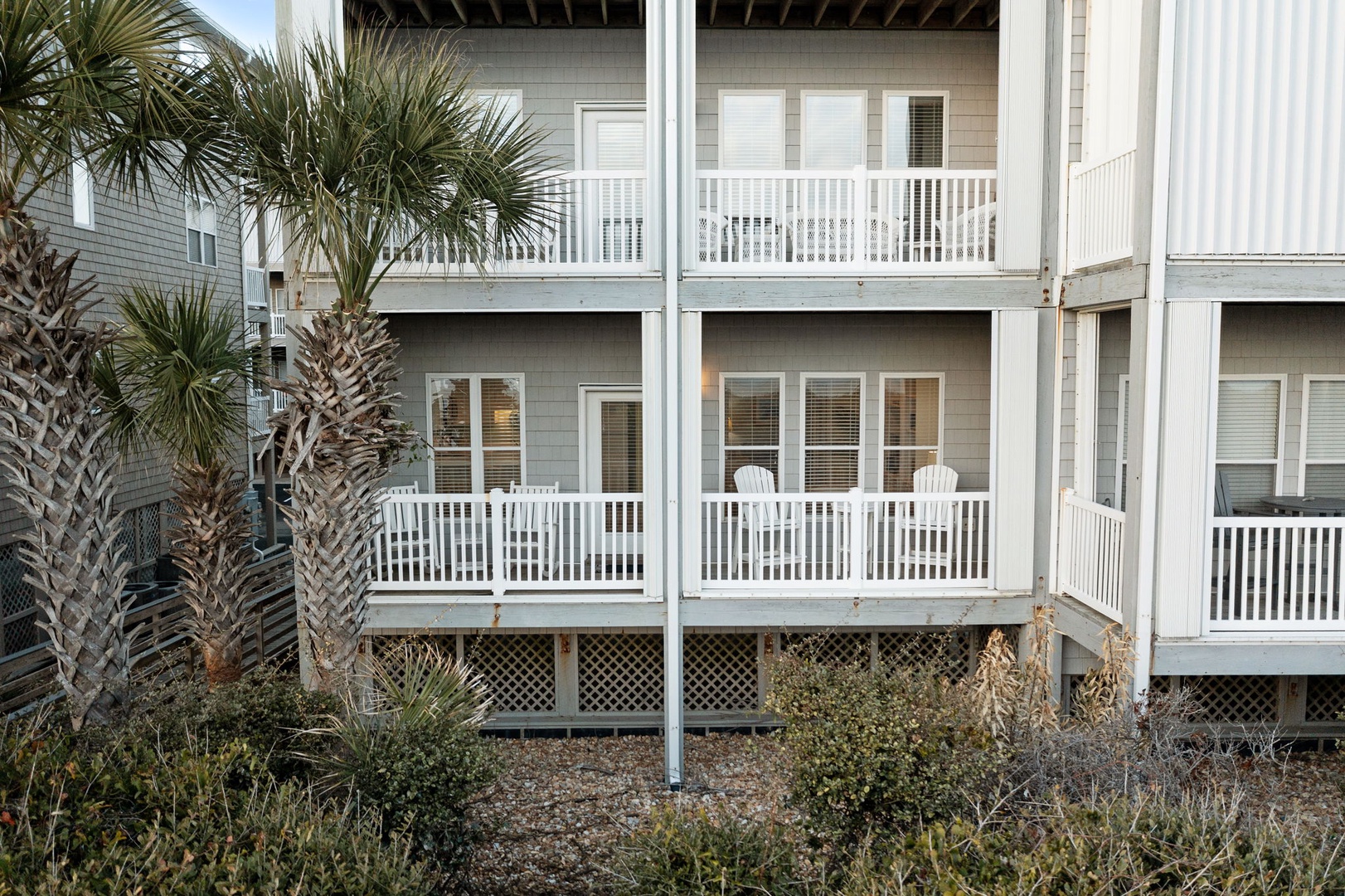 Coastal vacation rental with palm trees and private balconies featuring outdoor seating in a peaceful beachside setting.