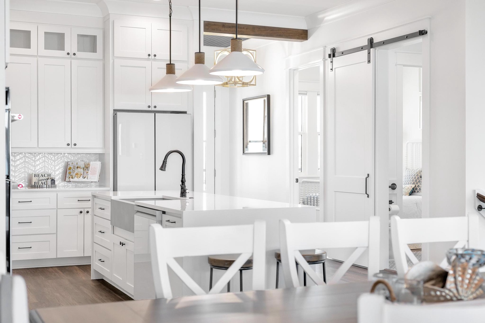Bright, open kitchen with modern appliances, pendant lighting, and a charming barn door inviting you to relax and cook your favorite meals in this airy coastal space.