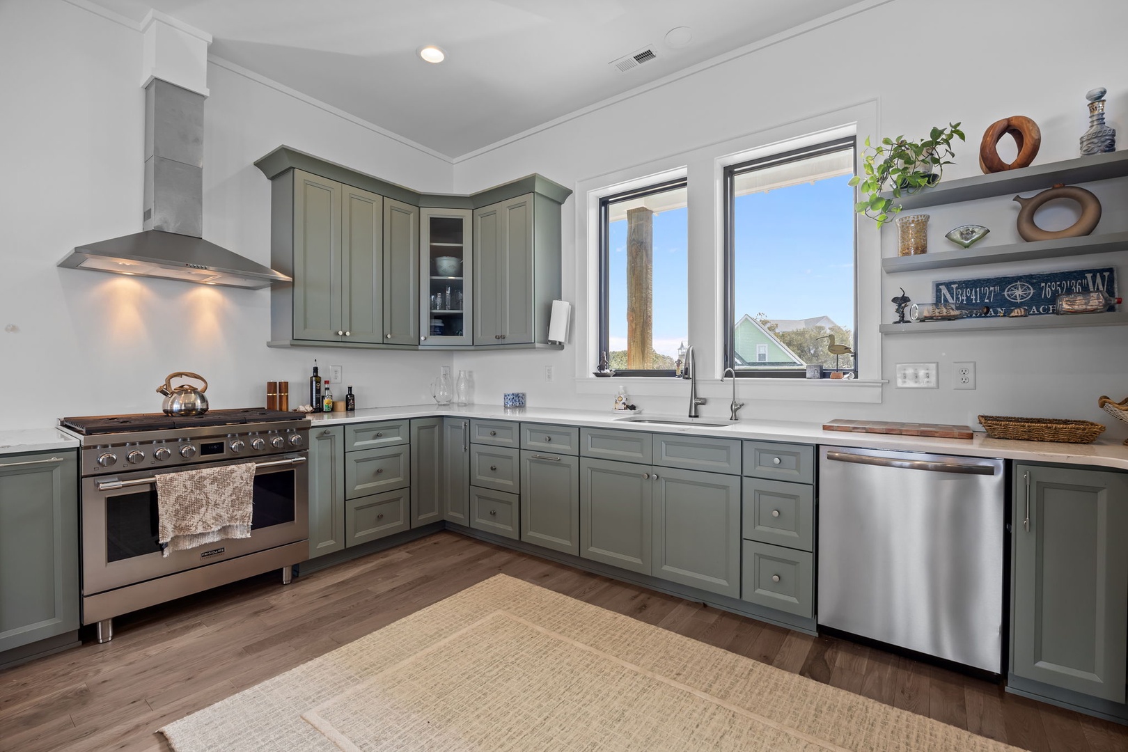 Your fully-equipped kitchen features sage green cabinets, stainless appliances, and windows that fill the space with natural light as you prepare meals.