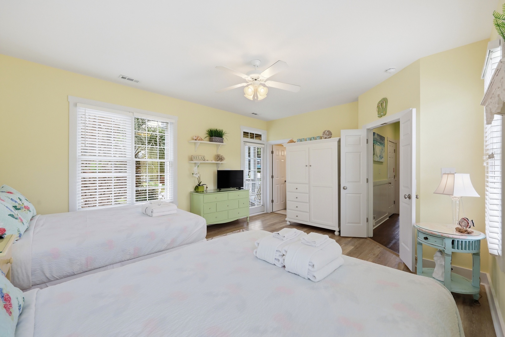 Unwind in your cheerful, sunlit bedroom with two cozy beds, ceiling fan, and ensuite bath. Fresh towels await you, and bright windows frame your peaceful retreat.