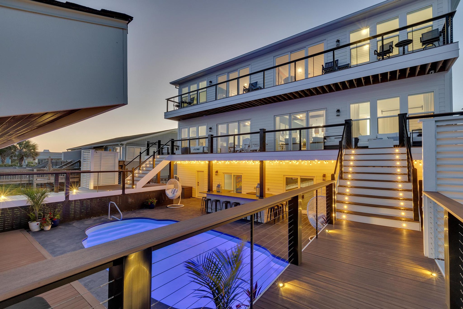 Modern beachfront vacation home featuring multiple decks, an inviting pool, and a welcoming outdoor bar area—perfect for coastal relaxation.