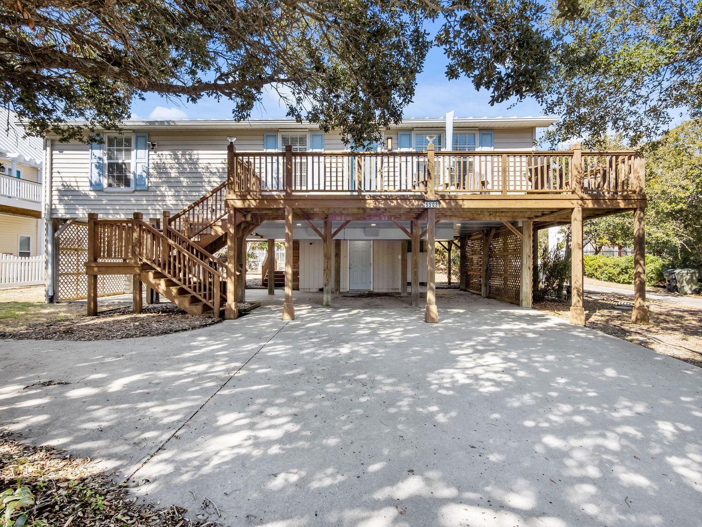 Elevated beach house with spacious deck and covered parking beneath mature trees.