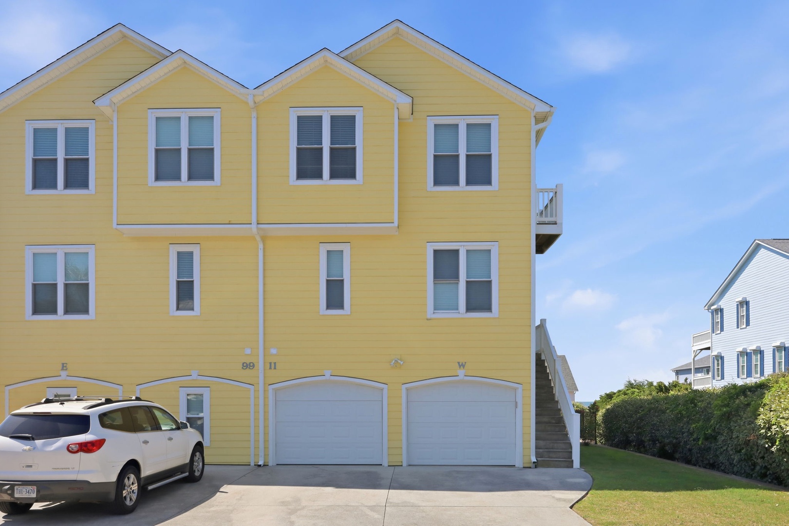 Cheerful yellow multi-unit beach property features ample parking and private garages, with an outdoor stairway leading to upper-level accommodations and nearby coastal access.