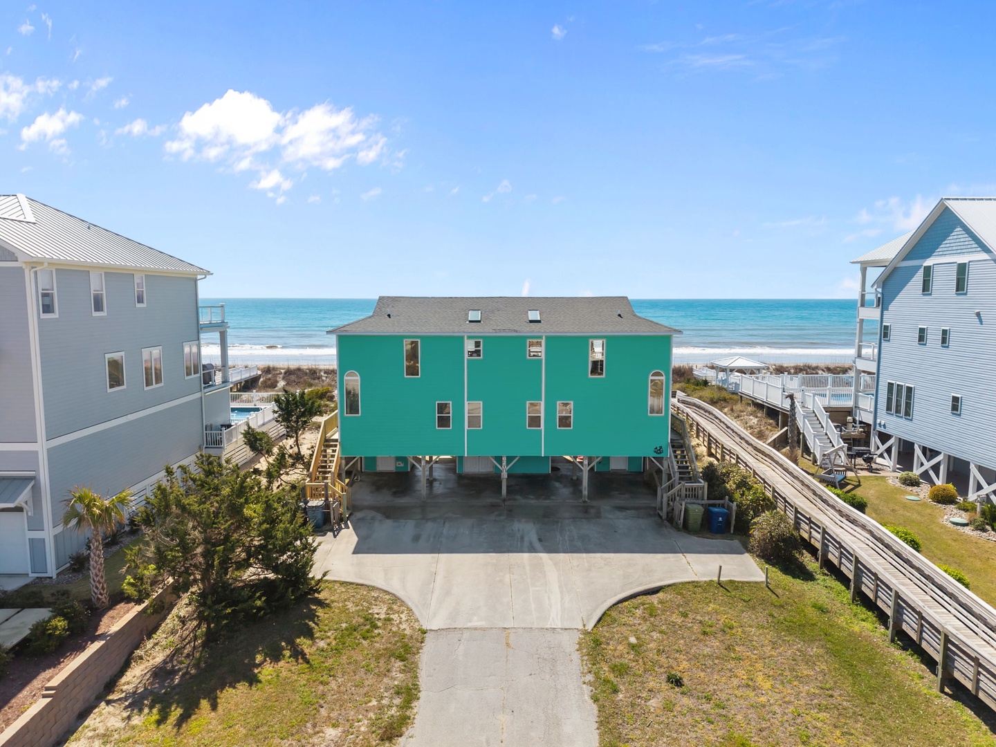 Bright turquoise beach house with ocean access, elevated on stilts with ample parking and boardwalk leading to pristine sandy shores.