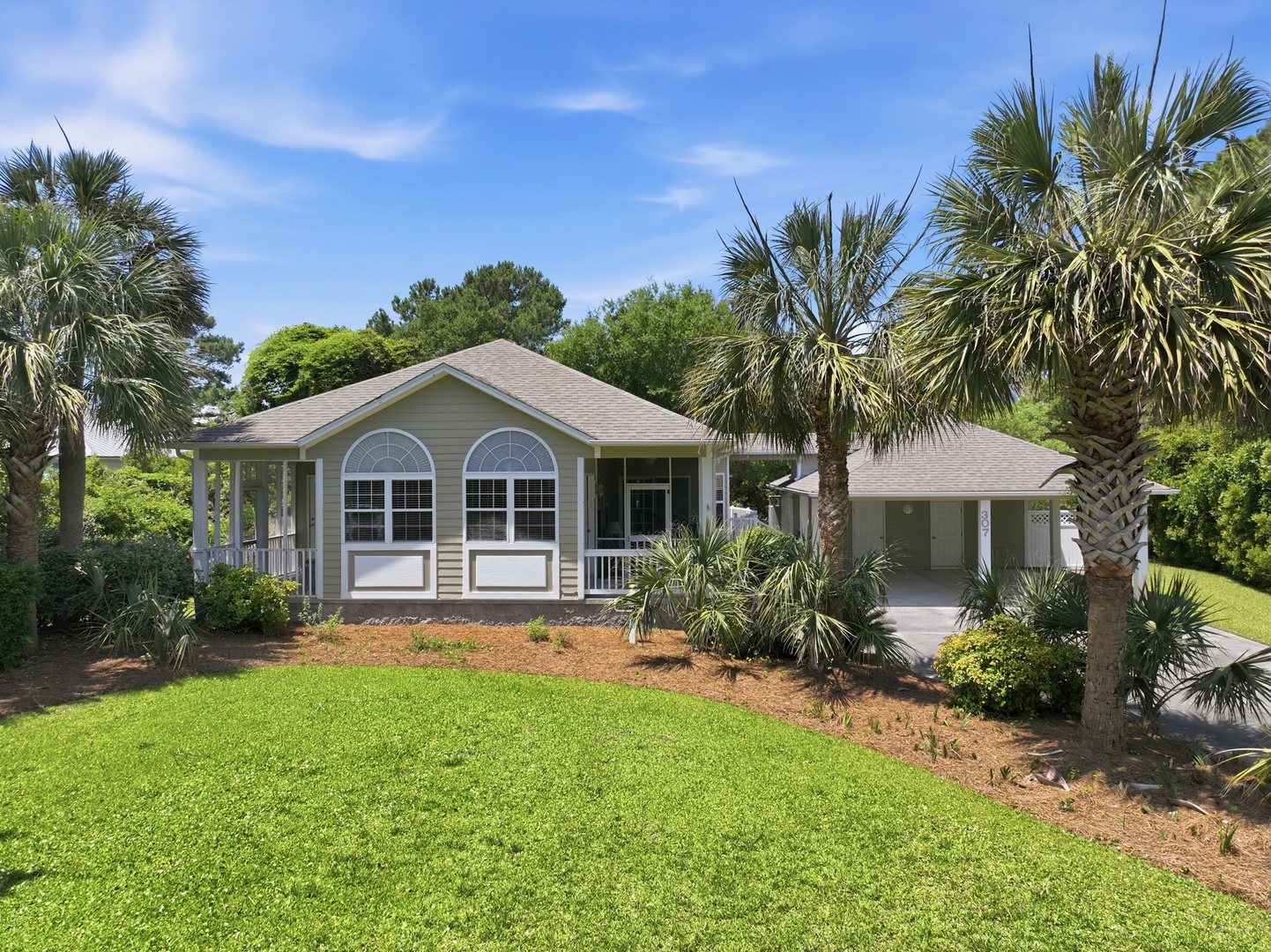 A charming single-story coastal home nestled among palm trees and lush greenery, offering a peaceful retreat with a screened porch and covered parking in a quiet neighborhood setting.