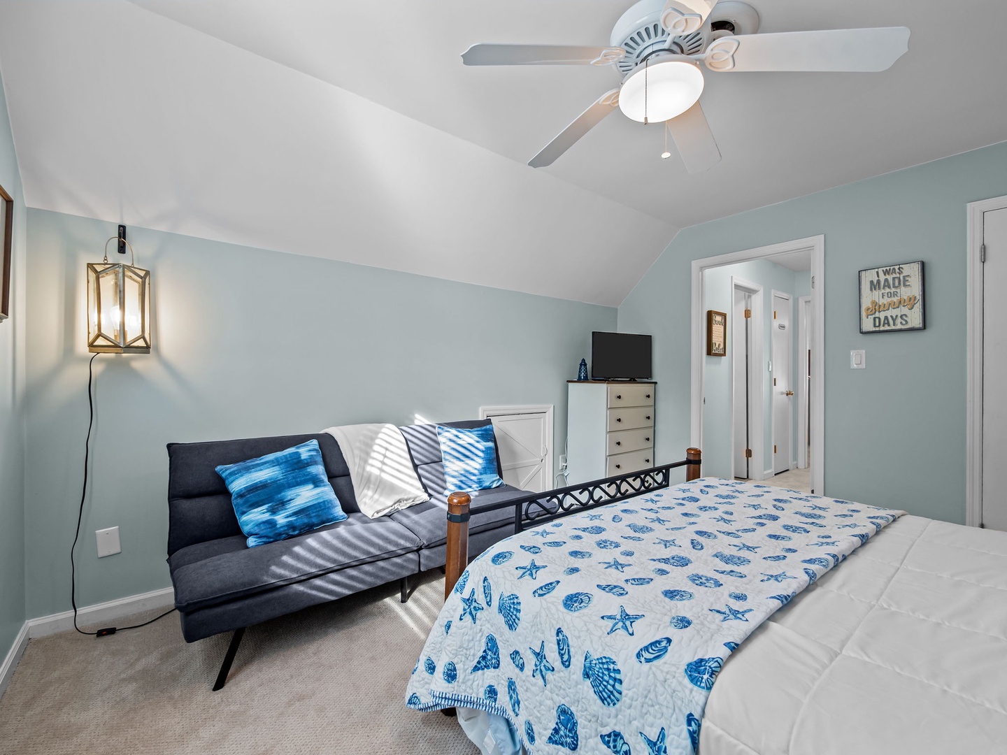 Drift off in this coastal-themed bedroom with soothing blue accents, comfortable seating area, and gentle ceiling fan for peaceful nights.