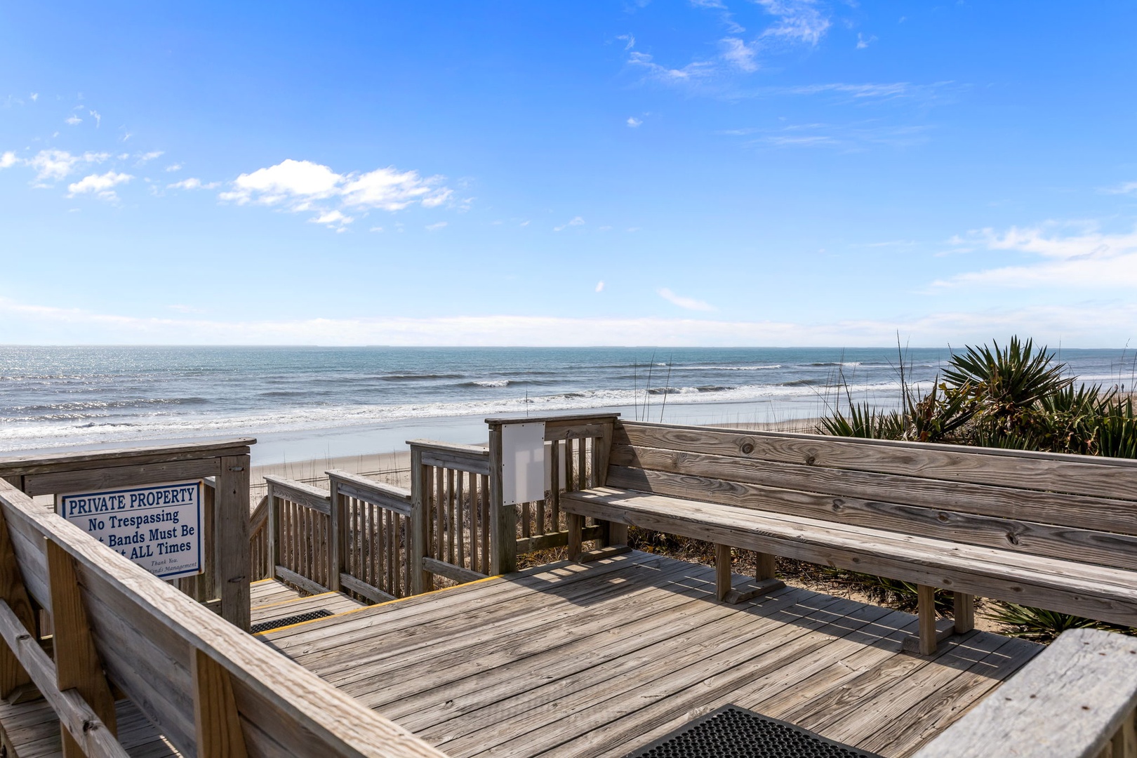 Wooden deck pathway leads directly to pristine beach with ocean waves and coastal vegetation, providing private beach access.
